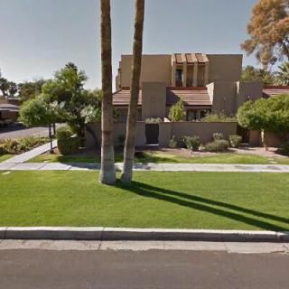 A suburban house with a well-maintained lawn and two tall palm trees casting long shadows.