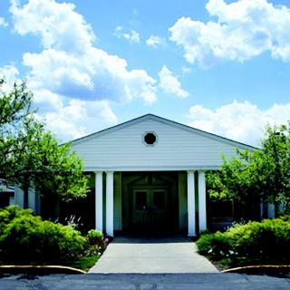 A building entrance with white columns and lush greenery under a partly cloudy sky.