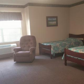 A cozy bedroom with two beds, a recliner chair, and a large window.
