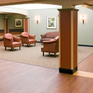 A cozy lobby area with chairs and a sofa arranged on a carpet, surrounded by a wooden floor and soft lighting.