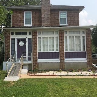 A charming two-story brick house with a landscaped front lawn and accessible pathway.