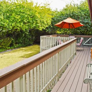 A spacious backyard featuring a wooden deck with outdoor furniture and an umbrella, surrounded by lush greenery.