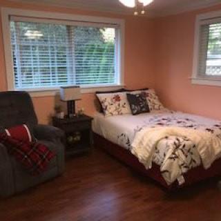 A cozy bedroom with a bed, armchair, and two large windows.