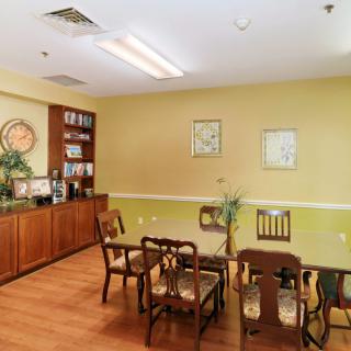 A cozy dining area with wooden chairs and table, decorated with wall art and a bookshelf in the corner.