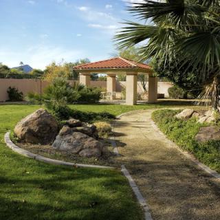 A serene garden featuring a paved pathway leading to a gazebo, surrounded by lush greenery and large rocks.