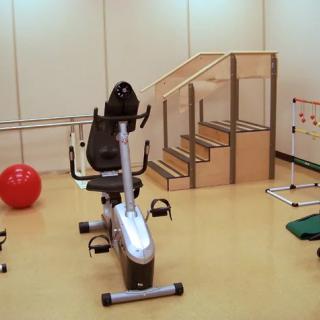 A rehabilitation room equipped with a recumbent bike, exercise ball, and therapy stairs.