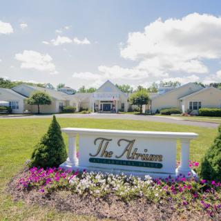 A landscaped area with a sign reading 'The Atrium' in front of a large building complex under a partly cloudy sky.