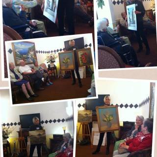 A group of people attending an art presentation, showcasing various paintings in a cozy indoor setting.