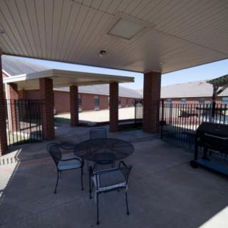 A covered patio with a table, chairs, and a grill next to a brick building.