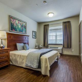 A cozy bedroom with a neatly made bed, featuring wooden furniture and a large window with curtains.