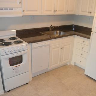 A compact kitchen with white cabinets and appliances, including a stove, sink, and refrigerator.