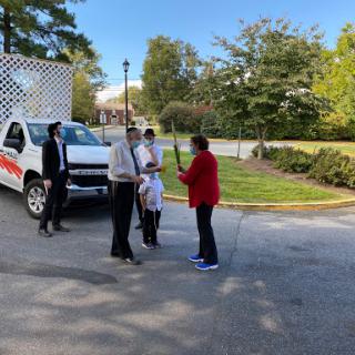 A group of people engaged in conversation near a truck in a green outdoor setting.
