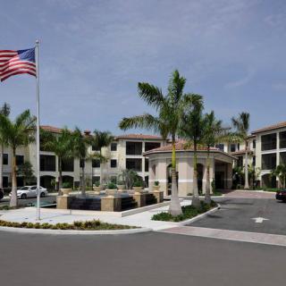 A building entrance surrounded by palm trees with an American flag flying nearby.