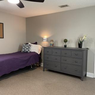 A minimalist bedroom with a single bed, dresser, and soft lighting.