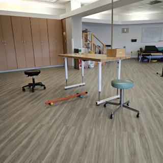 A spacious workplace featuring various types of furniture, including a standing table and rolling chairs.