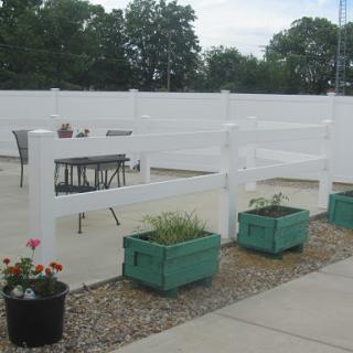 A serene outdoor space featuring a white fence, potted plants, and furniture for relaxing.