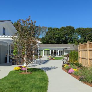 A beautiful garden pathway leading to a house with a wooden fence and vibrant flowers.