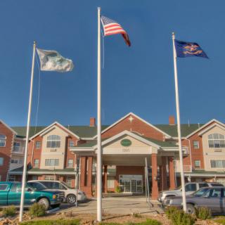 A hotel entrance with three flags and parked cars on a clear day.