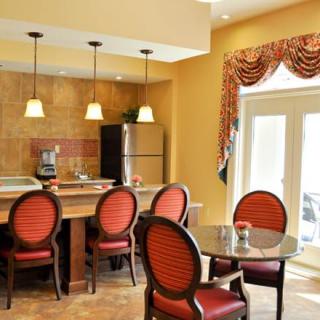 A cozy dining area with red cushioned chairs, a round table, pendant lighting, and a small kitchen with a refrigerator.