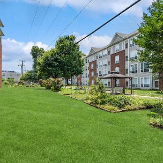 A serene residential landscape with well-maintained lawns and gardens, surrounded by apartment buildings under a clear blue sky.