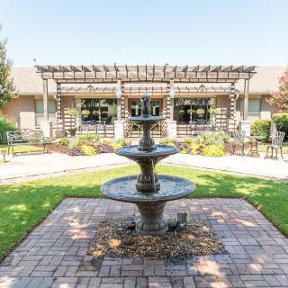 A picturesque courtyard with a central fountain and a surrounding garden featuring a pergola.