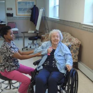 A nurse attends to an elderly woman sitting in a wheelchair during a medical appointment.