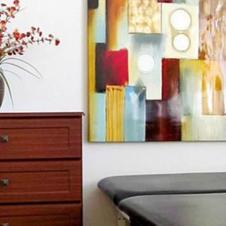 A room with an abstract painting above a drawer and a decorative plant.