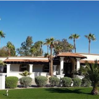 A Spanish-style house surrounded by palm trees and lush greenery under a clear blue sky.