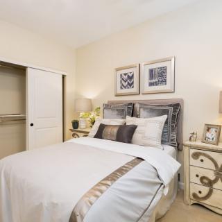 A cozy and elegantly furnished bedroom with a neatly made bed, decorative pillows, nightstands, and framed artwork on the wall.