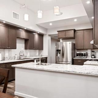 A modern kitchen featuring wooden cabinets, stainless steel appliances, and marble countertops with an island and pendant lighting.