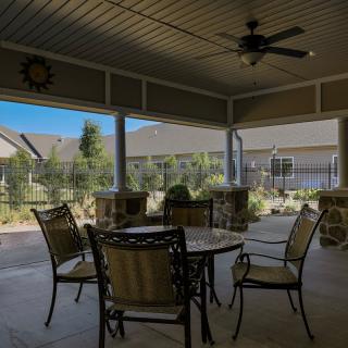 A covered patio with outdoor furniture, including a table and chairs, and a ceiling fan.