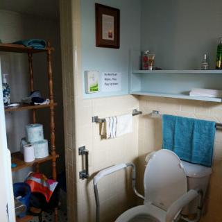 A cozy bathroom featuring a toilet, shelves with various items, and neatly arranged towels.