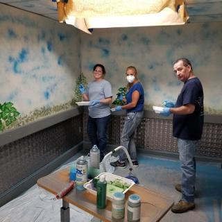 A group of three individuals working together to paint an artistic mural in a workshop.