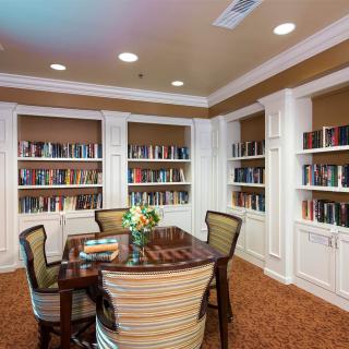 A cozy library room featuring a table and chairs surrounded by bookshelves filled with books.