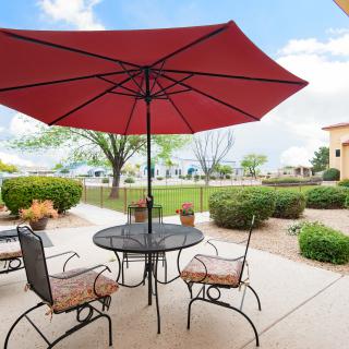 A patio with a red umbrella shading a table and chairs, surrounded by a landscaped garden on a sunny day.