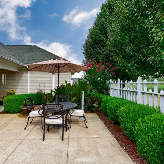A cozy patio with outdoor seating, surrounded by lush greenery and a white fence.