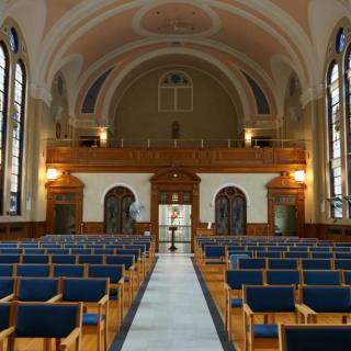 A serene chapel interior with rows of wooden pews and stained glass windows.
