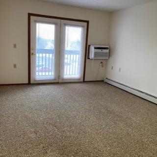 An empty living room featuring carpeted flooring and sliding doors that lead to an outdoor balcony.