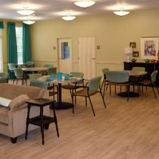 A spacious room featuring a seating area with tables, chairs, and a sofa. A piano is positioned in the corner, enhancing the cozy ambiance.