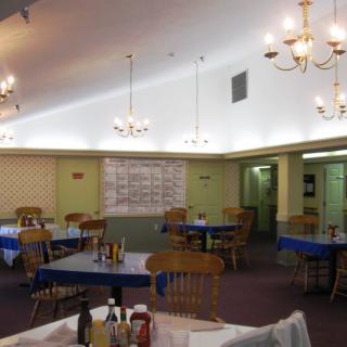 An empty restaurant dining room with wooden chairs and chandeliers.