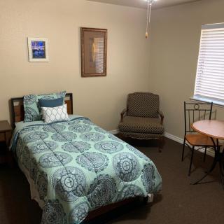 A cozy bedroom featuring a single bed with patterned bedding, an armchair, and a small table with a chair by the window.
