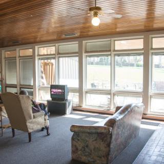 A bright and cozy living room featuring a floral sofa, an armchair, and a television, illuminated by natural light.