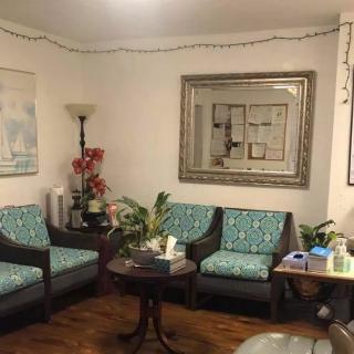 A cozy living room with a seating area, featuring patterned chairs, a table, and decorative elements like a lamp and plants.