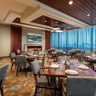 An elegant restaurant dining room with neatly arranged tables and chairs, featuring a fireplace and large windows.