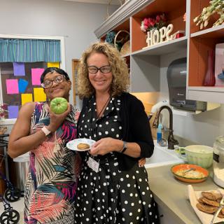 Two women enjoying a moment in the kitchen, one holding an apple and the other a plate of food.