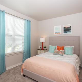 A cozy bedroom with pastel decor and natural light from a large window.