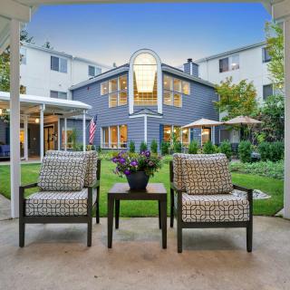 A cozy patio with two chairs and a table overlooking a garden and building.
