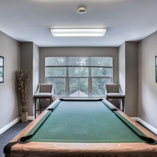 A cozy game room featuring a pool table, large window, and comfortable seating.