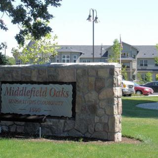 Stone sign at the entrance to a residential community with buildings and cars in the background.