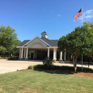 A well-maintained building featuring a United States flag, surrounded by lush greenery under a clear blue sky.